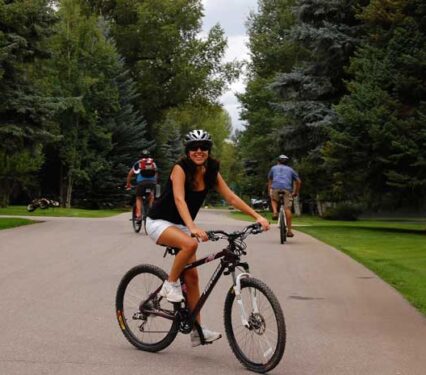 A girl smiling on a bike on a quiet Aspen, Colorado neighborhood street with two bicyclists riding past.